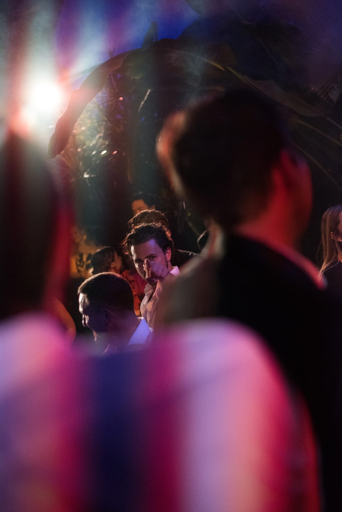 Invité en pleine conversation sur une piste de danse, lumières colorées et silhouettes au premier plan