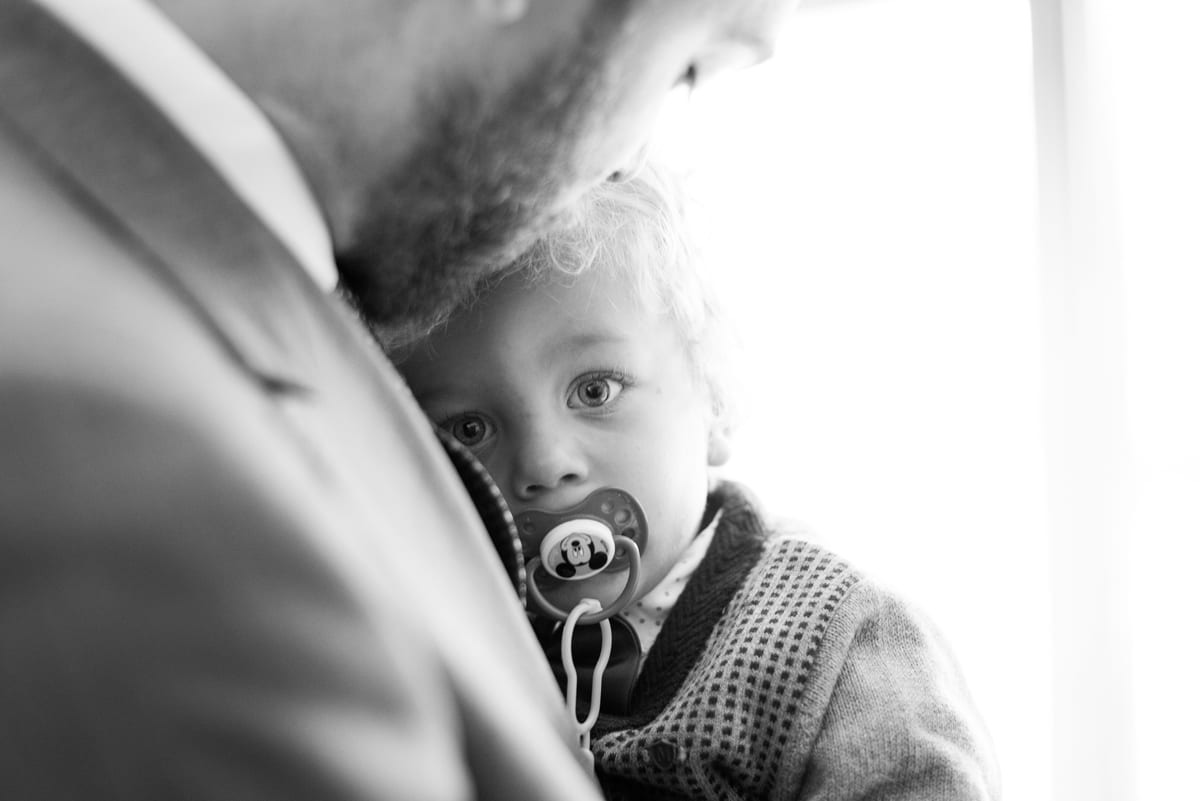 Jeune enfant à la tétine, blotti dans les bras d'un homme en costume, en noir et blanc